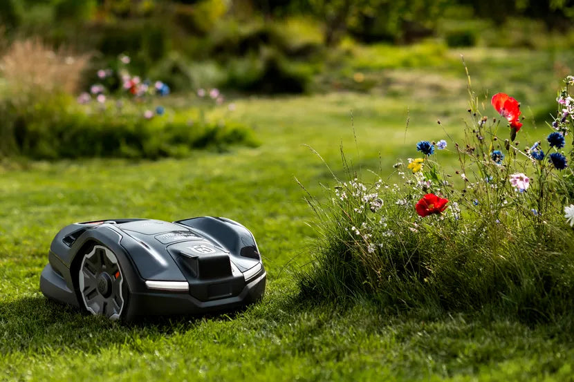 色とりどりの花の近くの庭で稼働するロボット芝刈り機。