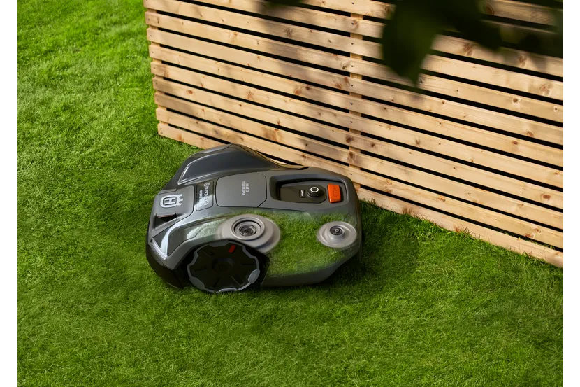 庭の木製フェンスの近くで稼働するロボット芝刈り機。